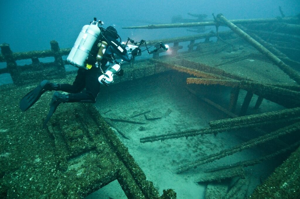 Nurek z aparatem fotograficznym dokumentuje zatopiony wrak na dnie morza – zdjęcie ilustracyjne NOAA, Unsplash